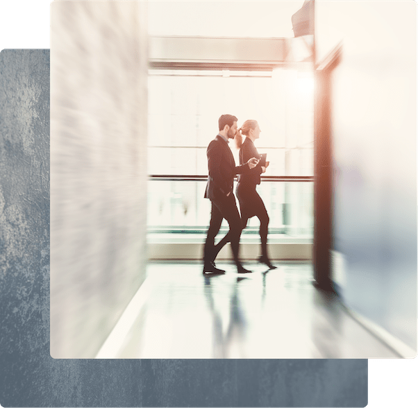 Two business professionals walking and talking in a bright, modern office hallway.