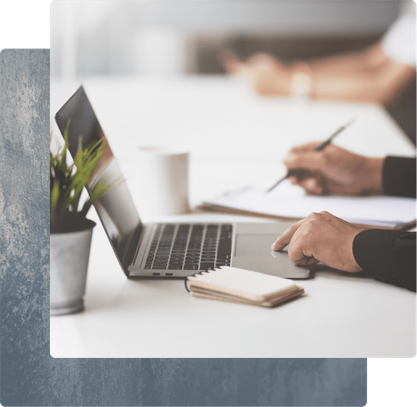 Close-up of hands multitasking with a laptop and a pen in a bright, modern office.