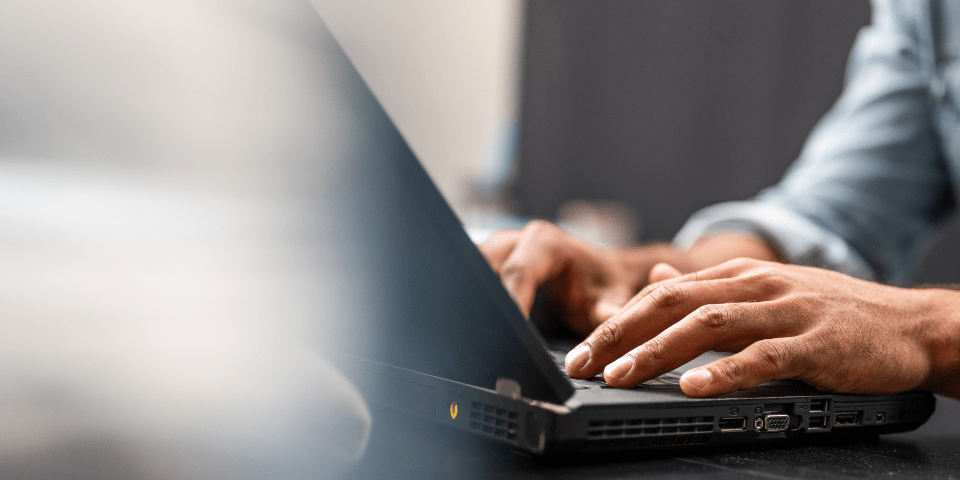 Close-up of a person's hands typing on a black laptop computer on a dark desk.