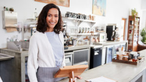 Woman standing behind the counter of a small coffee shop.