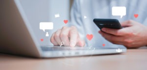 Closeup of person using a smartphone and laptop with hearts and conversation graphics overlay.